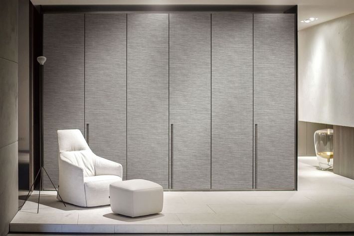 Cozy interior: White chair and ottoman in front of textured gray closet doors. Neutral color palette.
