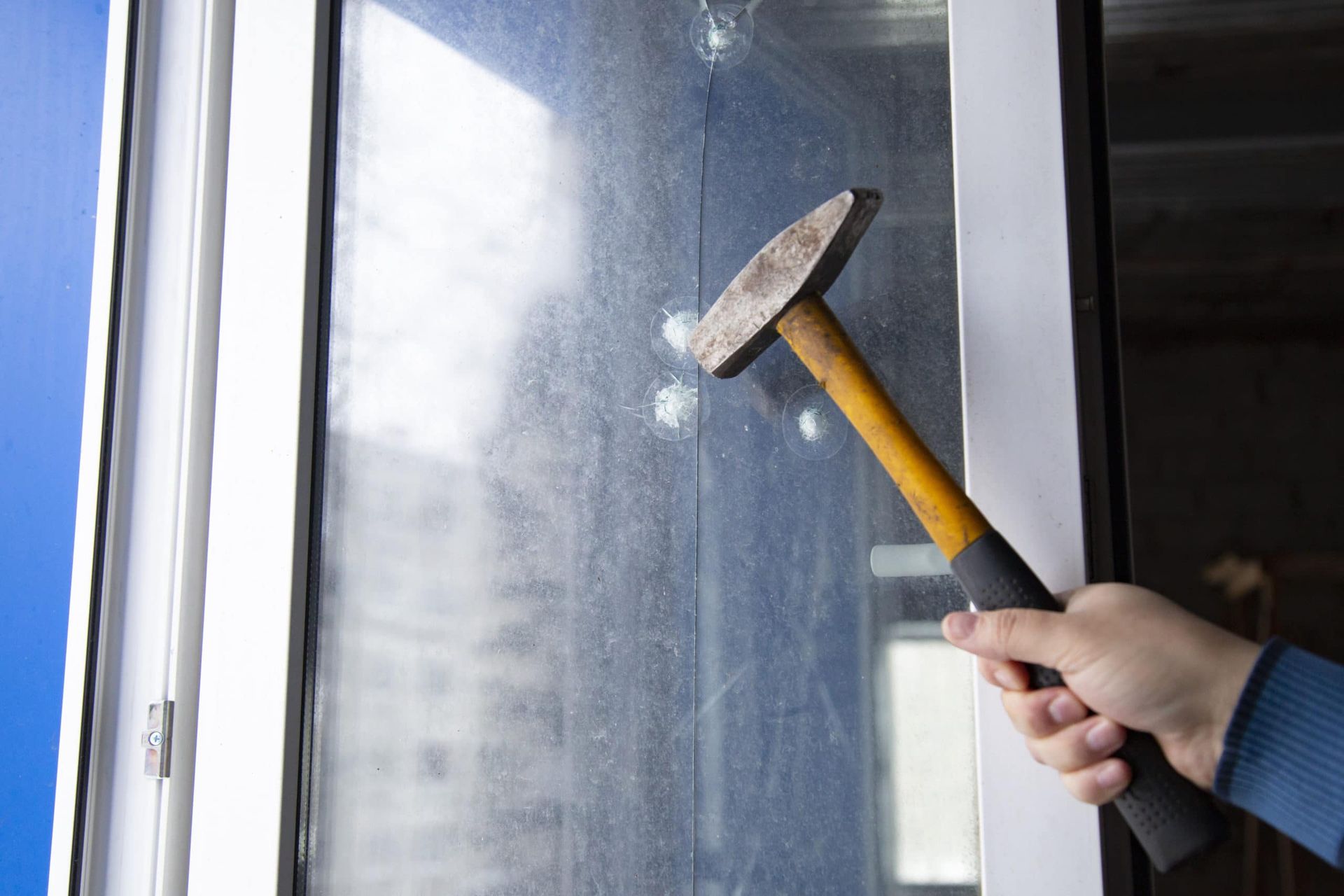 Hammer hitting a window; hand holding the hammer, smashing the glass.