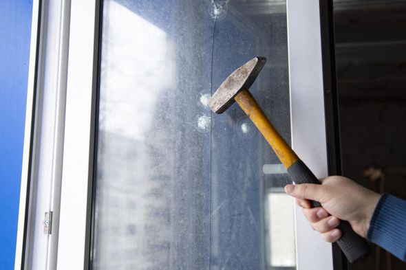 Hammer hitting a window; hand holding the hammer, smashing the glass.