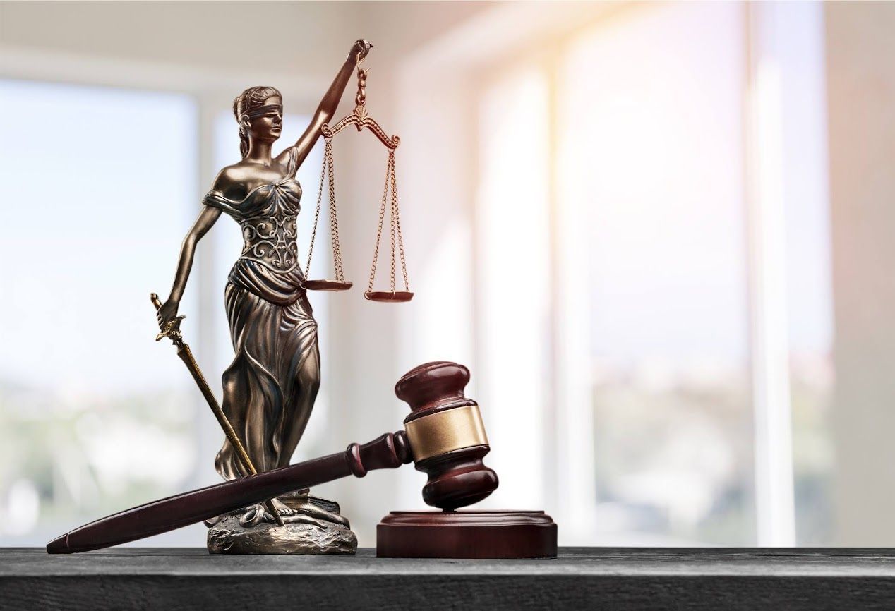 Una statua in bronzo della dea della giustizia che regge una bilancia e una spada, accanto a un martelletto da giudice in legno su un tavolo.
