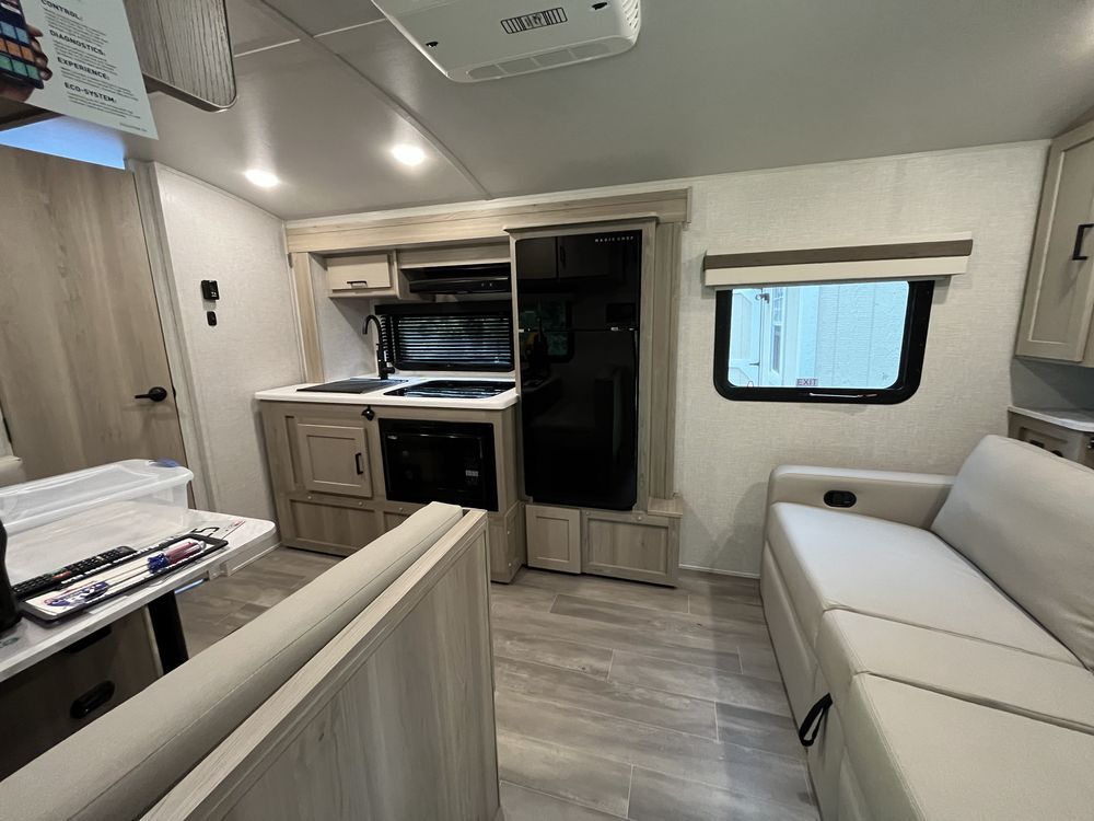Compact RV interior with kitchenette, fold-out bed, and white seating area.