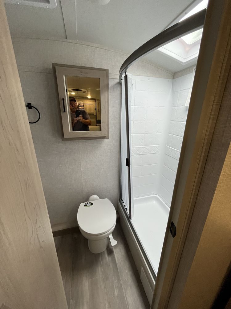 Small bathroom with toilet, glass shower, gray walls, wood-look floor, and mirror.