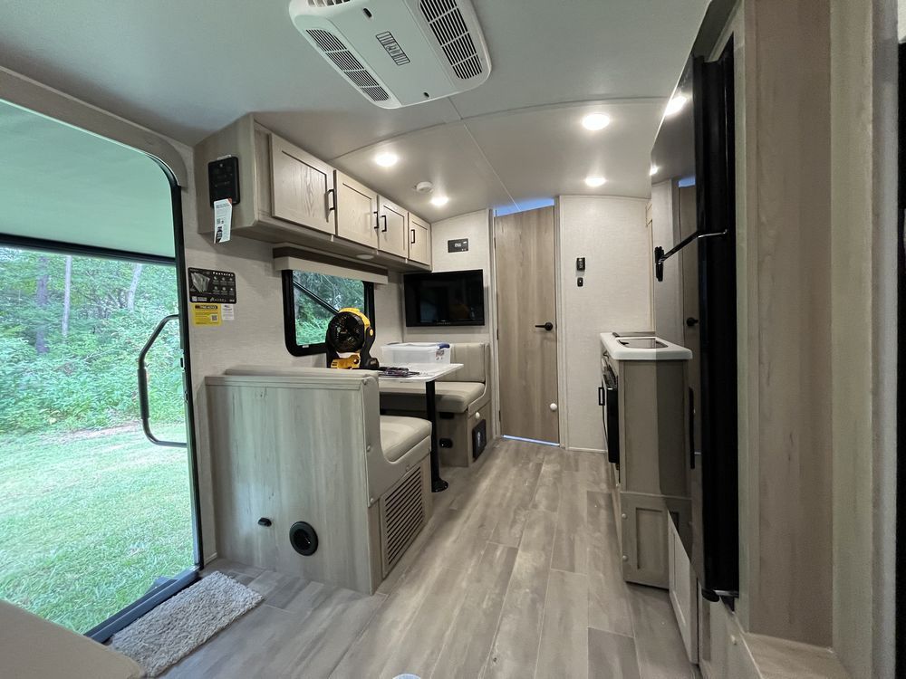 Modern RV interior with a compact kitchen, wood cabinets, and a sliding glass door to a green outdoor view