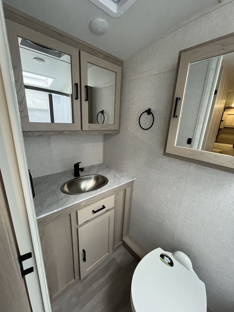 Small bathroom with vanity sink, mirror cabinet, towel ring, and toilet seat in view.
