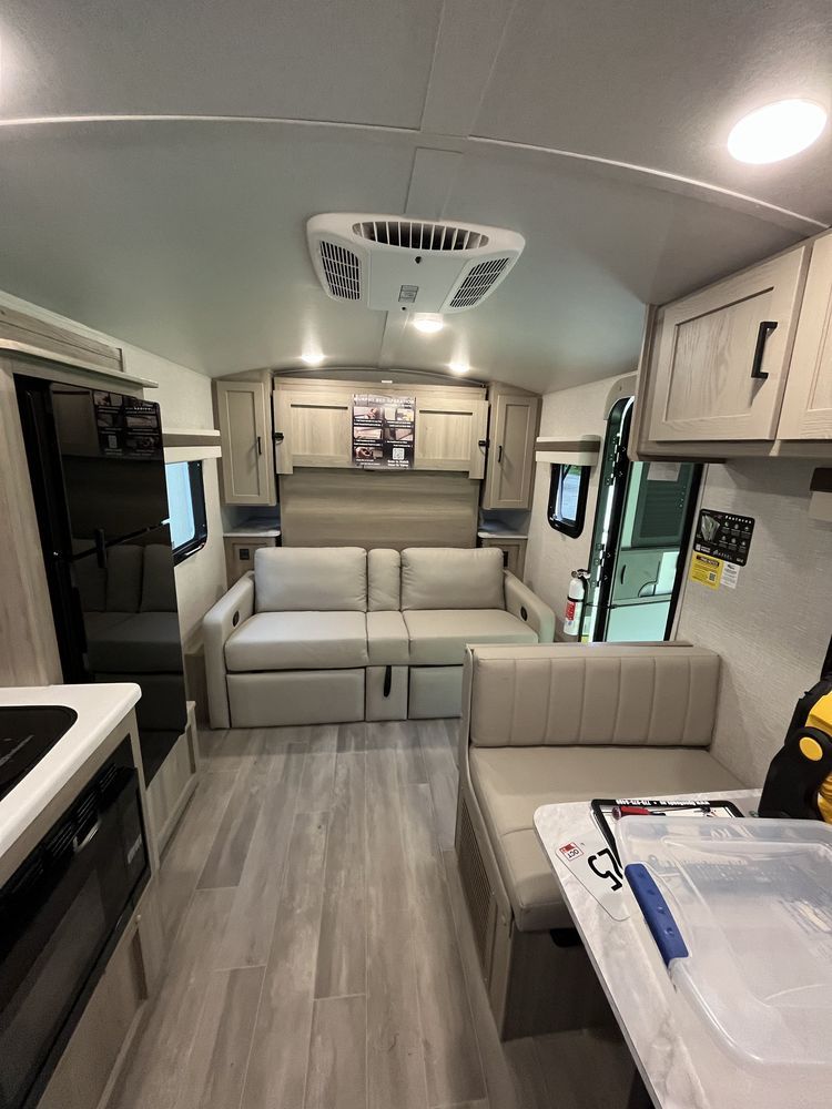 Modern RV interior with beige seating, light wood cabinets, and a central dining area
