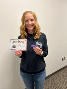 Smiling woman holding a “You Rock!” sign and a small item in a hallway