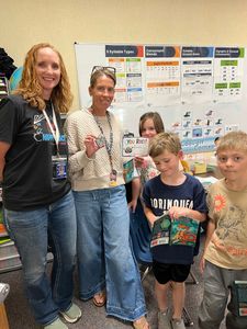 Five people pose smiling in front of a classroom poster display.