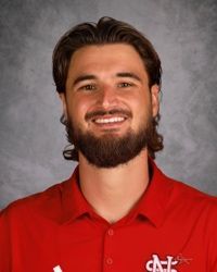 Smiling man in a red collared shirt against a gray studio backdrop