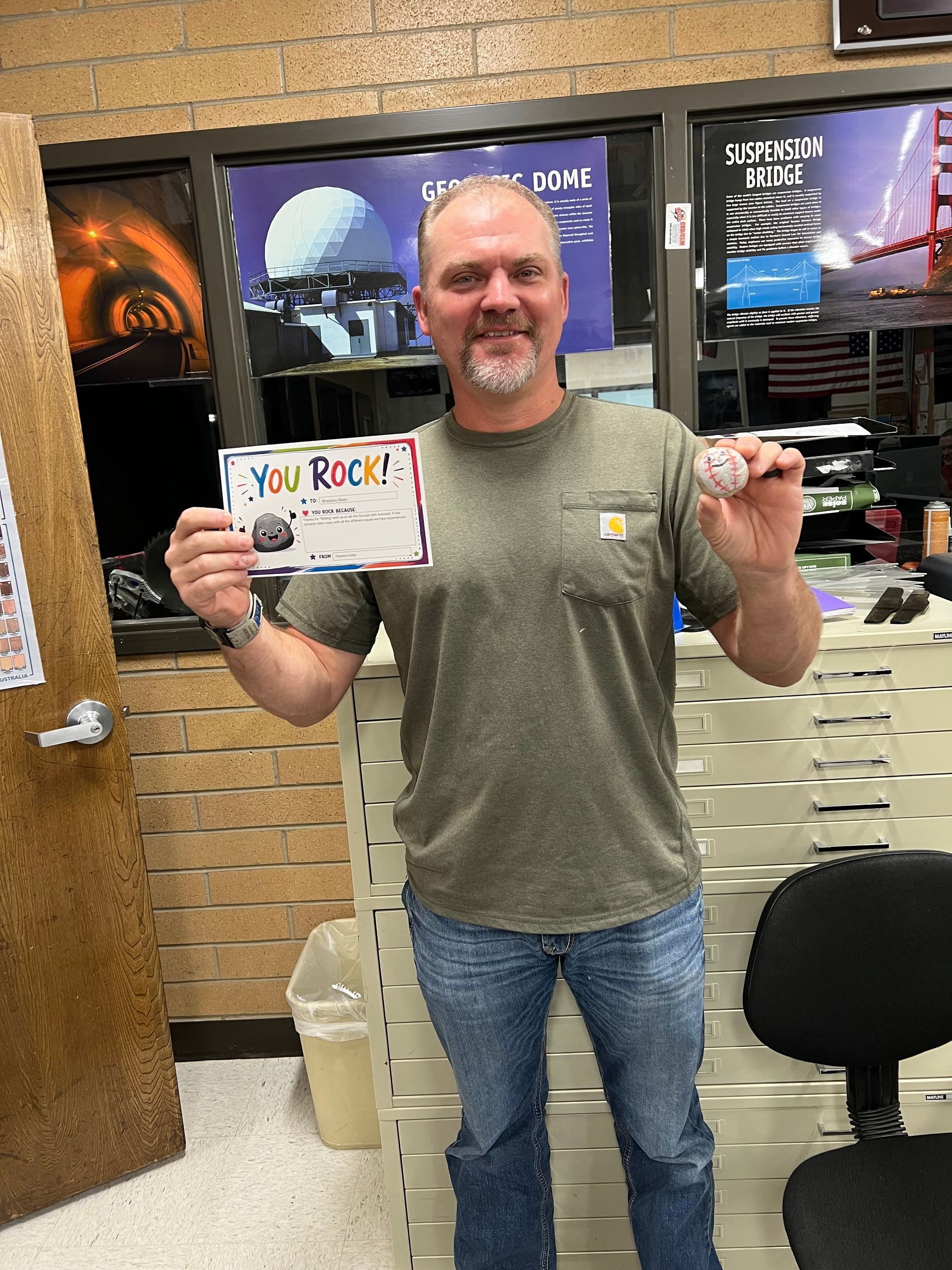 Man standing indoors, smiling and holding up a small card or ticket in both hands.