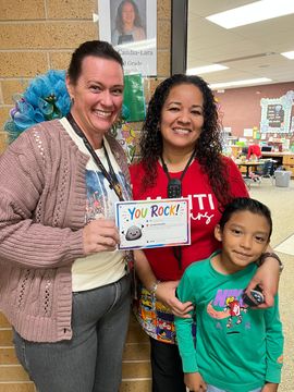 Two people and a child smiling, holding a “You Rock!” sign indoors.