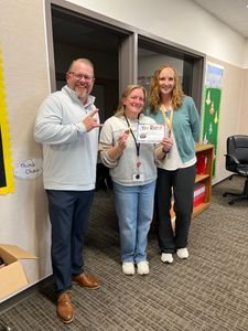 Three adults smiling and holding papers in a classroom hallway