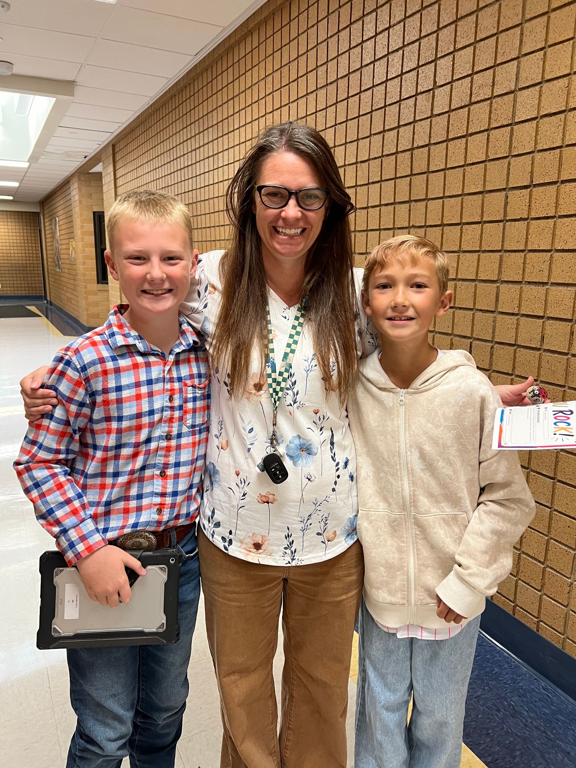 Three people standing in a school hallway, smiling at the camera.