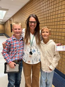 Three smiling people in a school hallway, standing together with a tablet and papers.