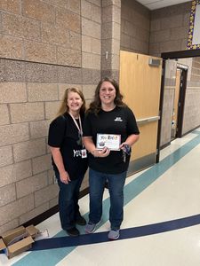 Two people standing in a school hallway, smiling and holding a certificate.