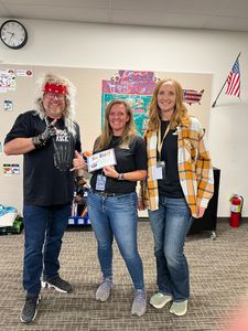 Three people posing indoors with certificates, smiling in a classroom-like setting.