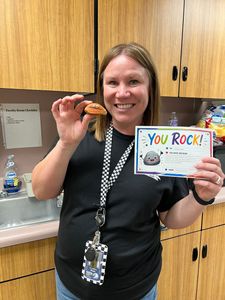 Smiling woman in a classroom holding a pastry and a “You Rock!” card