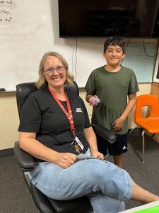 Woman seated in an office chair beside a boy standing near a desk and TV screen