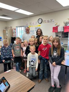 Group of children and an adult standing in a classroom, posing for a photo.