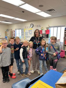 Teacher and smiling children posing together in a bright classroom with colorful posters and desks