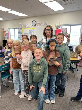 Group of smiling children and a teacher standing together in a classroom, holding a small brown object