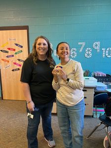 Two people smiling and holding a small trophy in a classroom with a teal wall and chairs