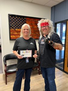 Two people in a room, smiling and holding a small award plaque, with an American flag artwork on the wall.