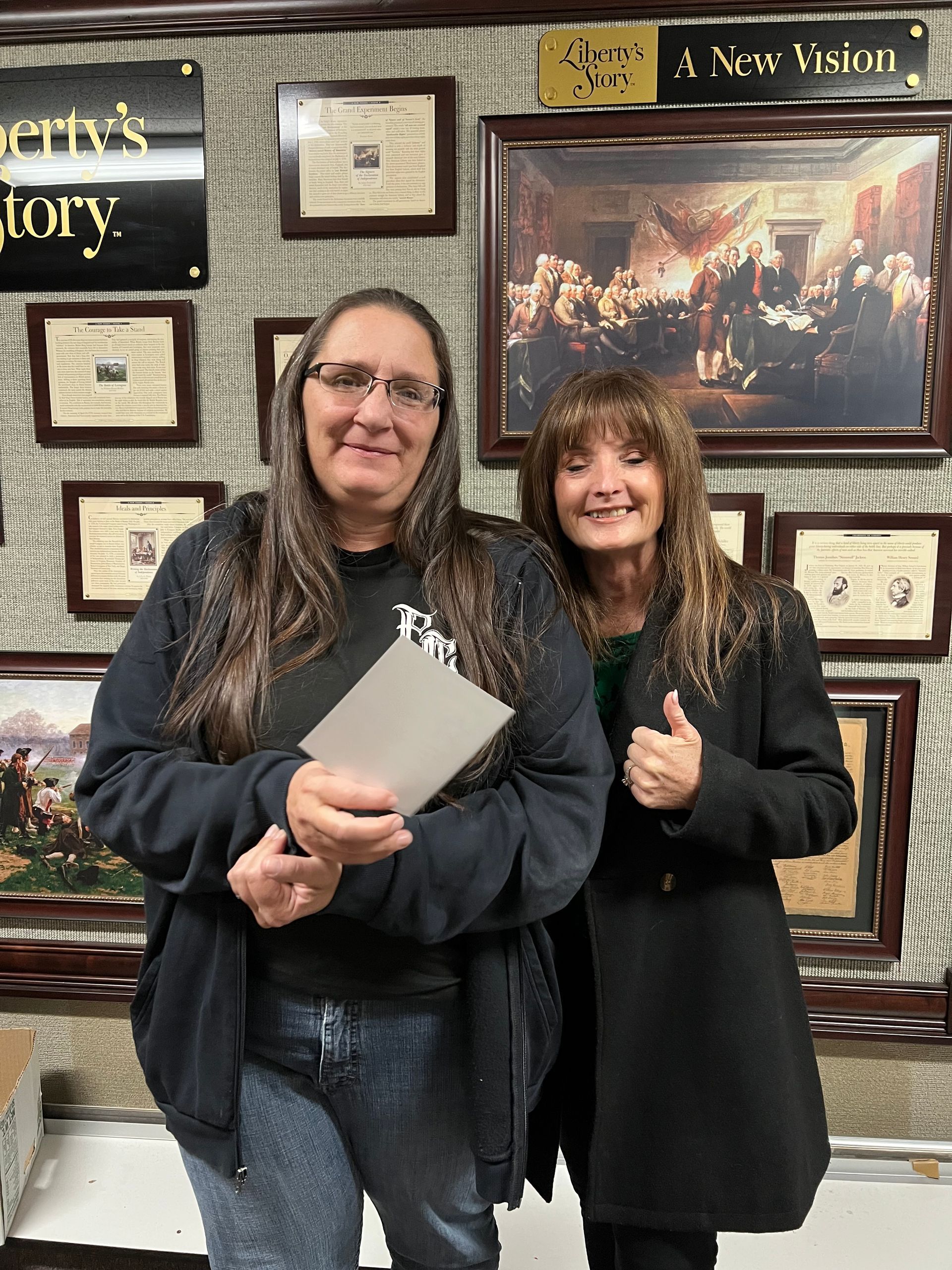 Two women are standing next to each other in a room holding a card.