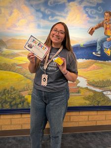 Smiling person holding a certificate and yellow prize in front of a colorful mural backdrop