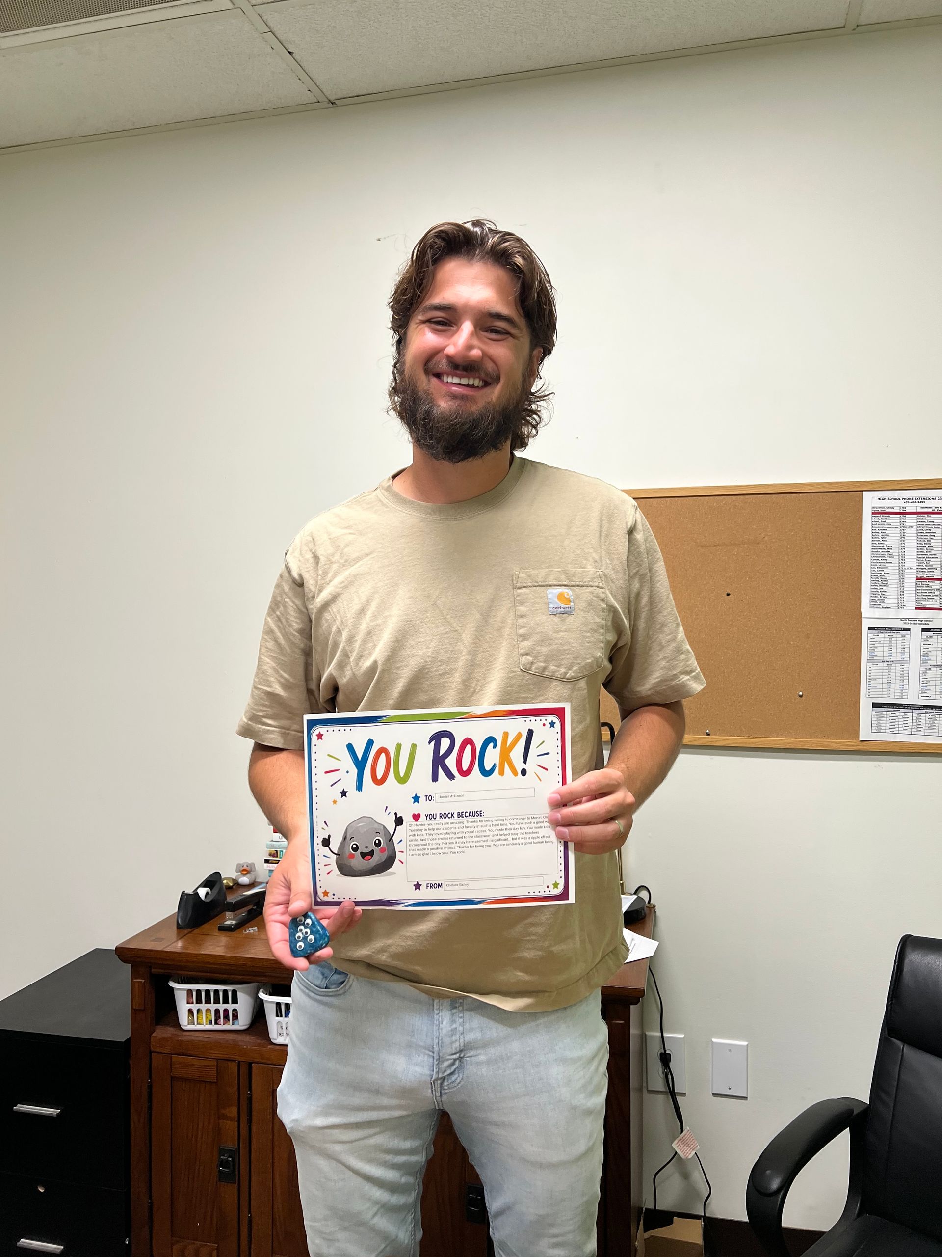 Smiling man standing in an office, holding a colorful “You Rock!” sign.
