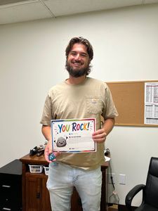 Man smiling and holding a colorful “You Rock!” sign in an office room.