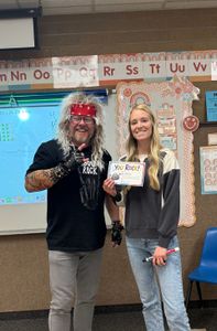 Two people smiling in a classroom, holding a certificate together.