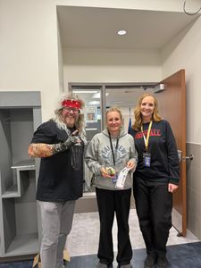 Three people posing indoors at a doorway, smiling and holding a small trophy.