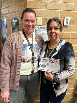 Two women smiling in a hallway, holding a “You Rock!” sign.