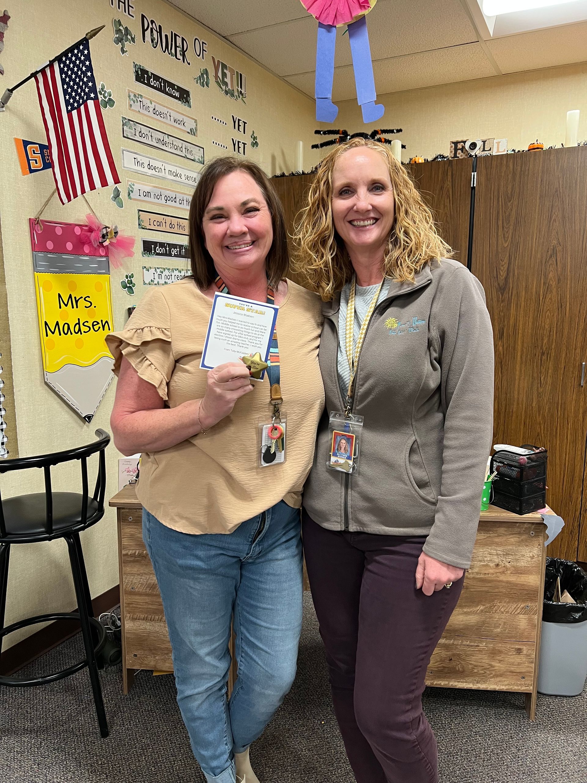 Two women are standing next to each other in a room holding a piece of paper.