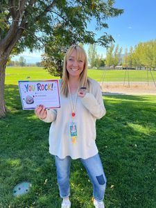 Woman outdoors holding a “You Rock!” sign under a tree on a sunny day