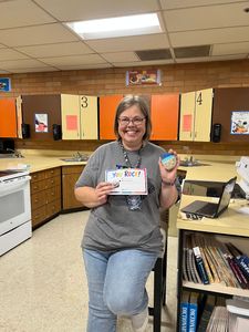 Person smiling in a classroom, holding a certificate and a small trophy.