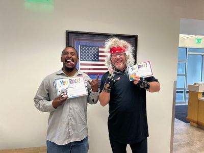 Two smiling people holding You Rock signs in front of a framed American flag indoors