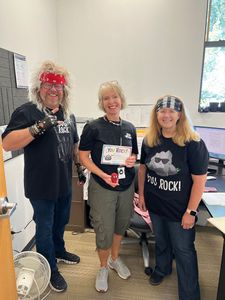 Three people posing indoors, one holding a certificate, in black band T-shirts and festive headwear.