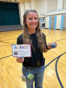 Person smiling in a gym, holding a “You Rock!” sign and a blue ribbon