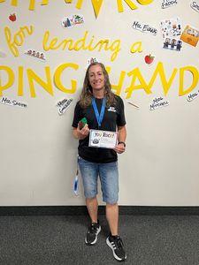 Woman holding a certificate and medal, standing in front of a colorful wall mural.