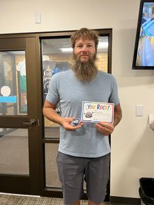 Man standing indoors holding a colorful book, near glass doors and a wall-mounted screen.