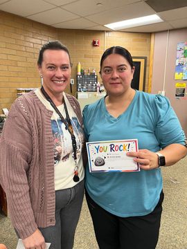 Two smiling people holding a “You Rock!” certificate in an indoor hallway