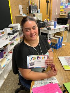 Person in a classroom holding a “You Rock!” card and smiling at the camera.