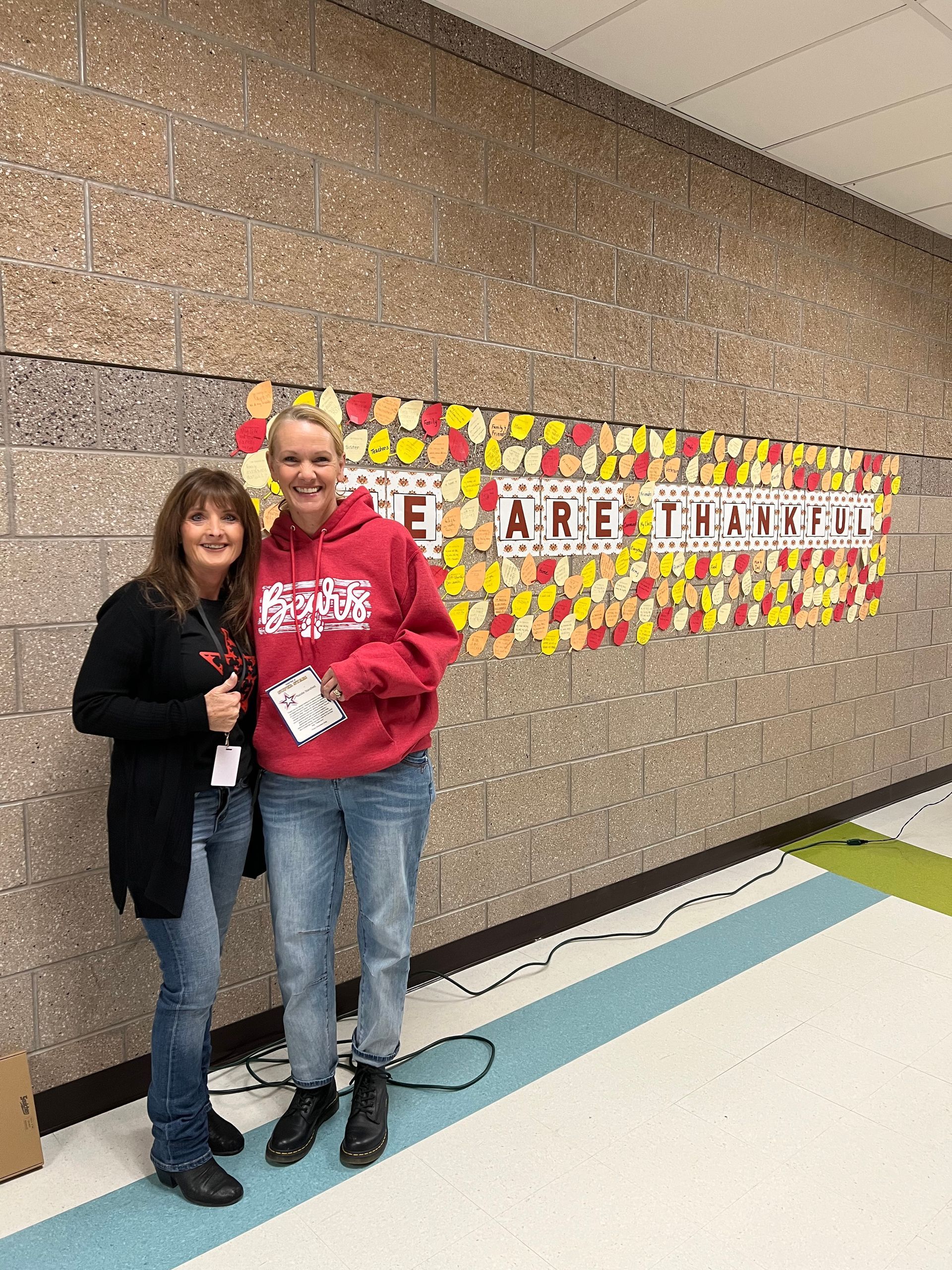 Two women are posing for a picture in a hallway . one of the women is wearing a blue shirt.