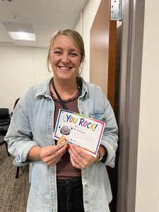Smiling woman holding a colorful “You Rock!” card in a hallway