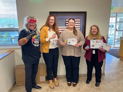 Four people smiling indoors, holding certificates and gift cards in a lobby.