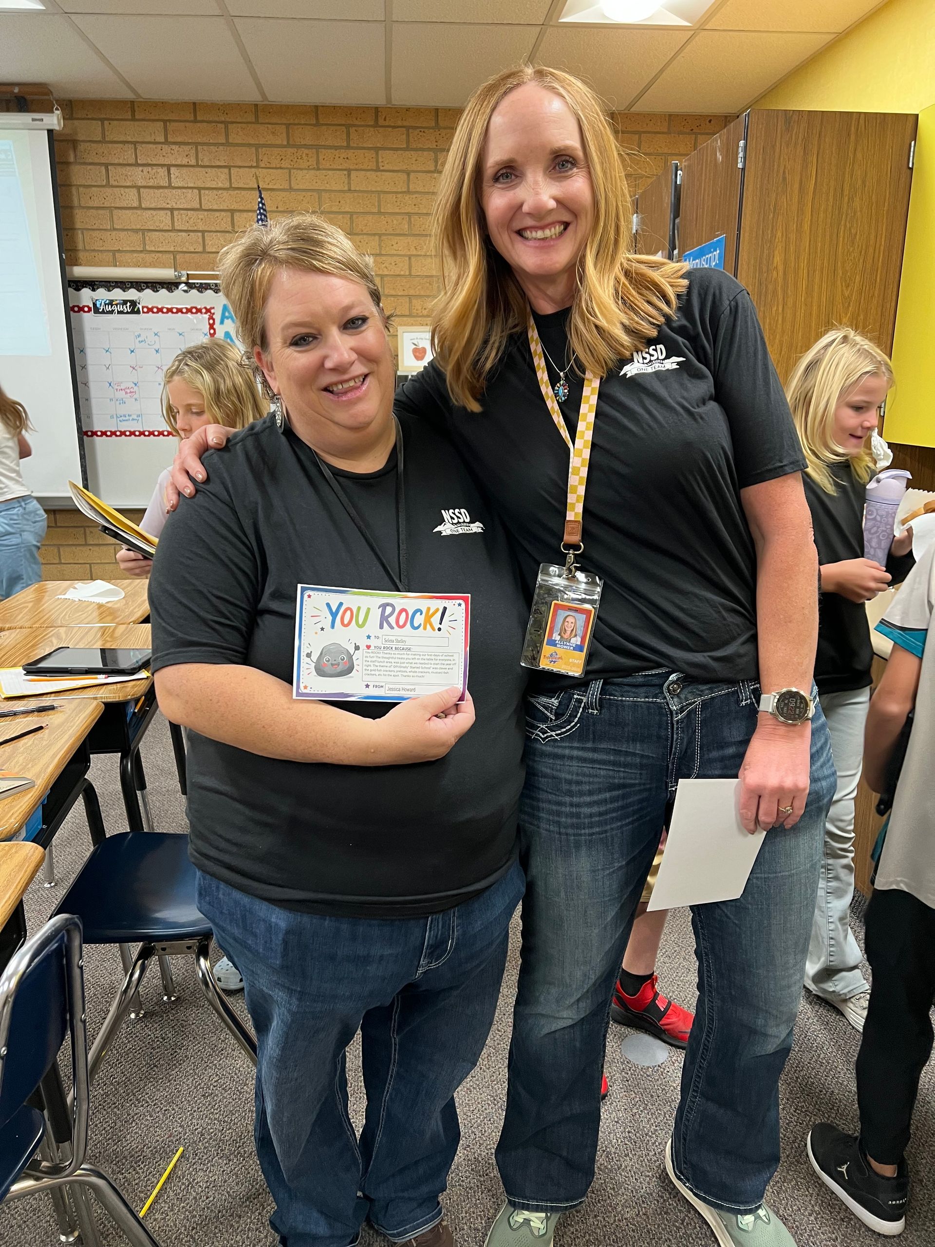 Two women smiling in a classroom, holding a small award box.