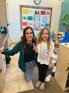 Woman and child smiling in a classroom, standing by a bulletin board and doorway.