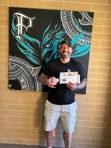 Man standing indoors holding a certificate in front of a teal-and-black decorative wall mural