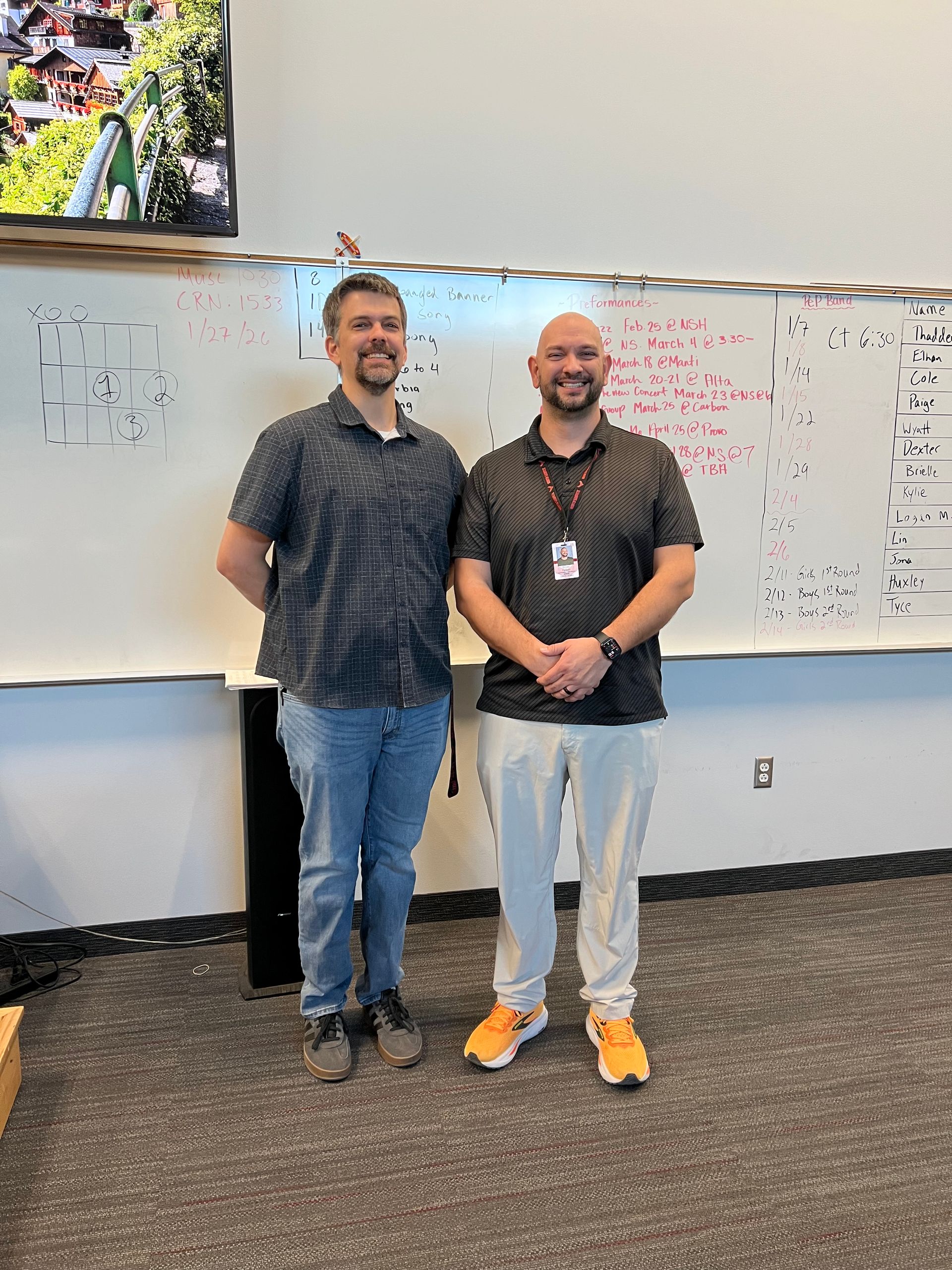 Two men are standing next to each other in a classroom holding a book.